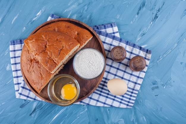 Half of fresh white bread with raw egg and flour on a tablecloth .