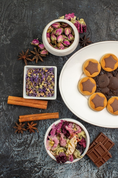 Half left view of a plate of cookies with dry flowers and cinnamons and chocolates on grey ground
