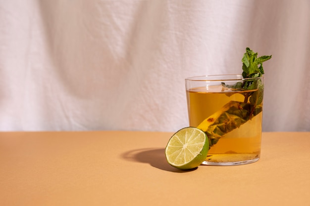 Free photo half lemon with cocktail drink arranged on brown desk in front of white curtain