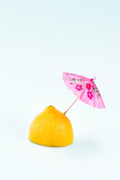 Half of lemon with pink umbrella on top on light background
