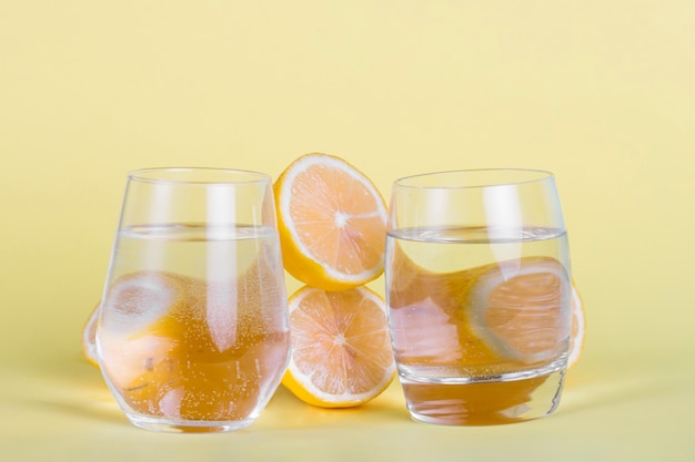 Бесплатное фото Половина лимонов и стаканов воды на желтом фоне