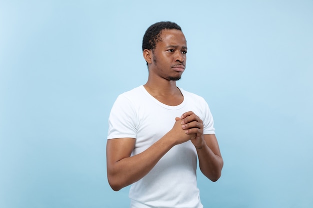 Mezzo busto vicino ritratto di giovane modello maschio afro-americano in camicia bianca sulla parete blu. emozioni umane, espressione facciale, concetto di annuncio. dubbi, chiedere, mostrare incertezza, premuroso.
