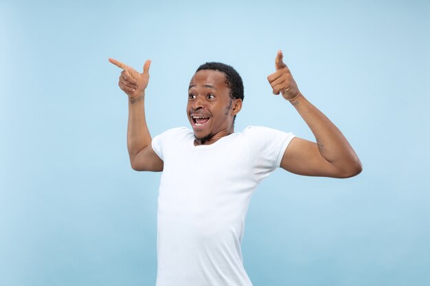 Half-length close up portrait of young african-american man in white shirt on blue background. Human emotions, facial expression, ad, concept. Celebrating, wondered, astonished, shocked, crazy happy.