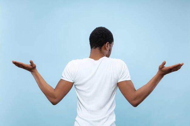 青いスペースに白いシャツを着た若いアフリカ系アメリカ人男性のハーフレングスのクローズアップの肖像画。人間の感情、表情、広告、販売コンセプト。不確実性、疑い