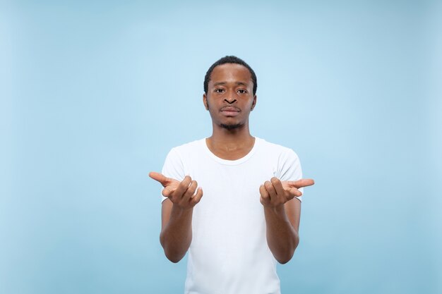 Half-length close up portrait of young african-american man in white shirt on blue space