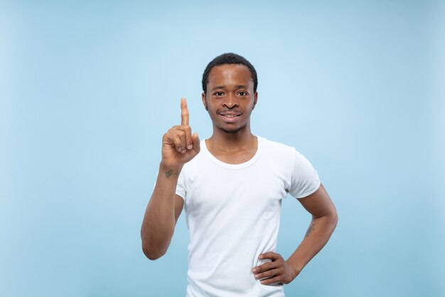 Half-length close up portrait of young african-american man in white shirt on blue space