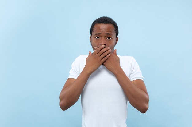 Half-length close up portrait of young african-american man in white shirt on blue space