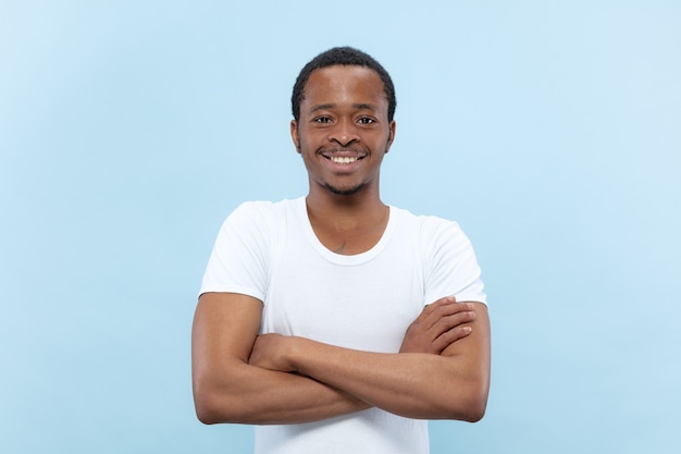 Half-length close up portrait of young african-american man in white shirt on blue space
