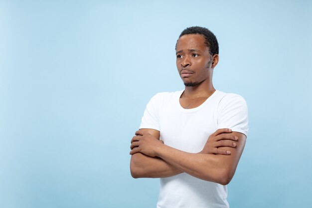 青いスペースに白いシャツを着た若いアフリカ系アメリカ人男性のハーフレングスのクローズアップの肖像画。
