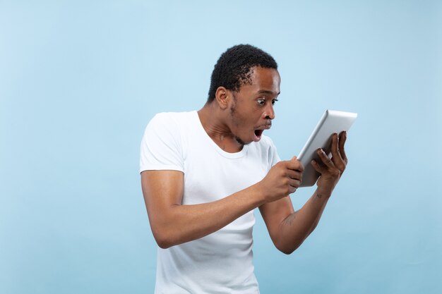 Half-length close up portrait of young african-american man in white shirt on blue space