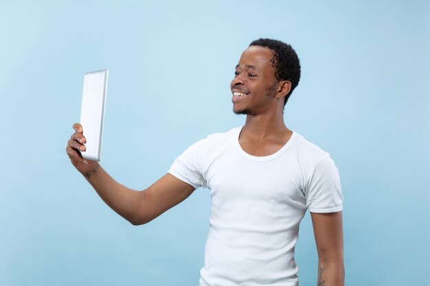 Half-length close up portrait of young african-american man in white shirt on blue space