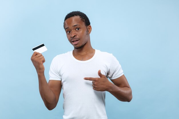 Half-length close up portrait of young african-american man in white shirt on blue space