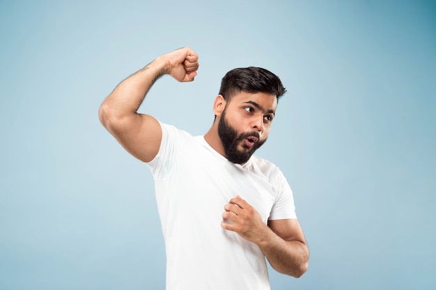 Free photo half-length close up portrait of young hindoo man in white shirt on blue background. human emotions, facial expression, ad concept. negative space. celebrating, winning, crazy happy.