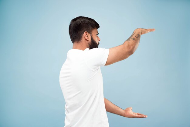 Half-length close up portrait of young hindoo man in white shirt on blue space