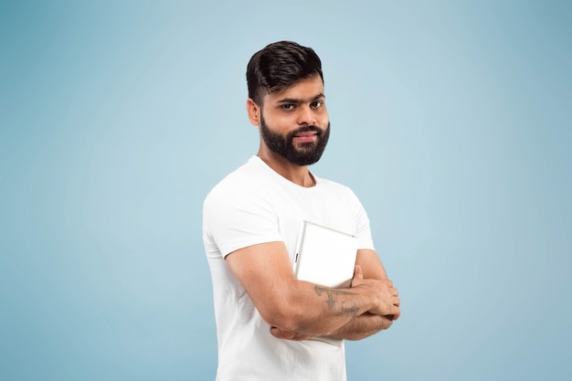 Half-length close up portrait of young hindoo man in white shirt on blue space