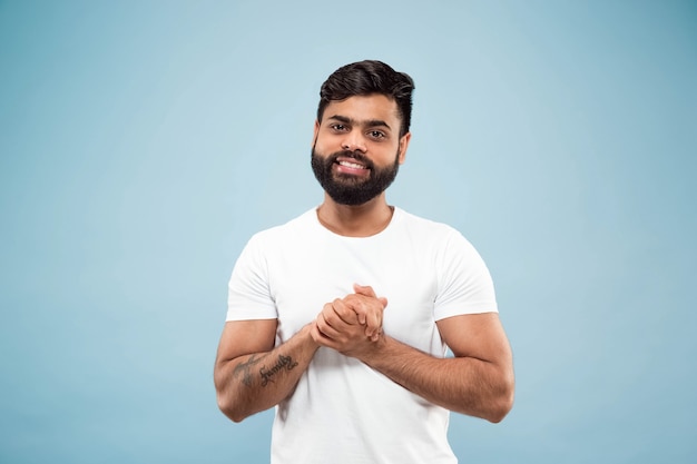 Half-length close up portrait of young hindoo man in white shirt on blue space