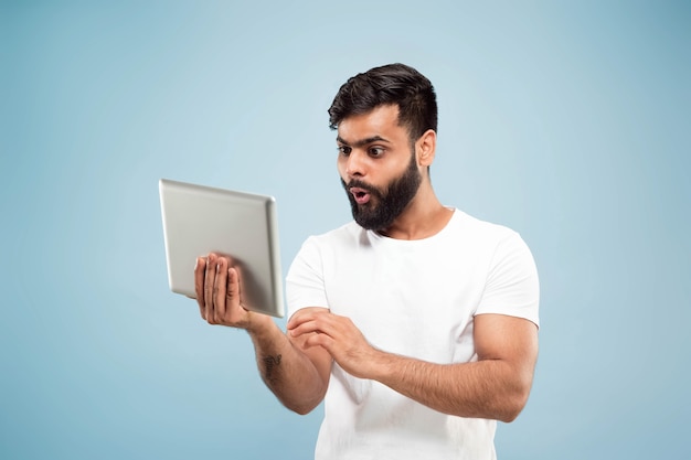 Half-length close up portrait of young man on blue wall.