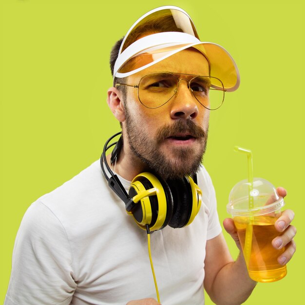 Half-length close up portrait of young man in shirt. Male model with headphones and drink. The human emotions, facial expression, summer, weekend concept. Getting serious.