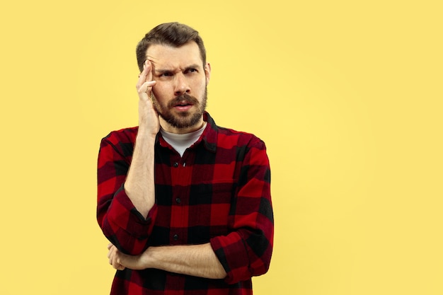 Half-length close up portrait of young man in shirt on yellow space. The human emotions, facial expression concept. Front view. Trendy colors. Negative space