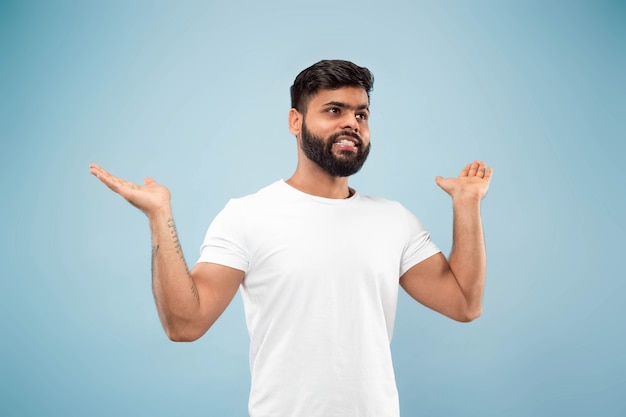 Half-length close up portrait of young man in white shirt on blue wall