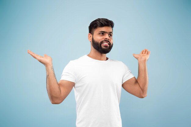 Half-length close up portrait of young man in white shirt on blue wall