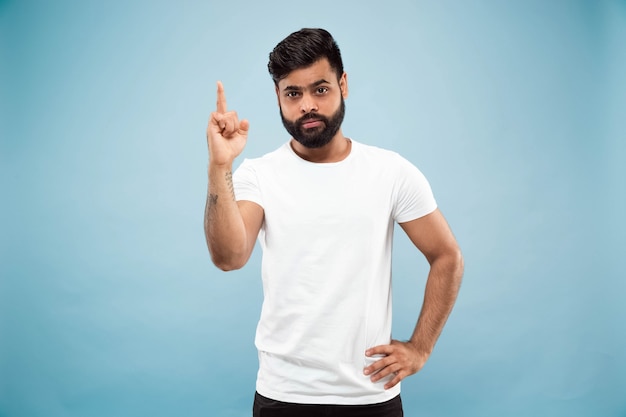 Half-length close up portrait of young man in white shirt on blue wall