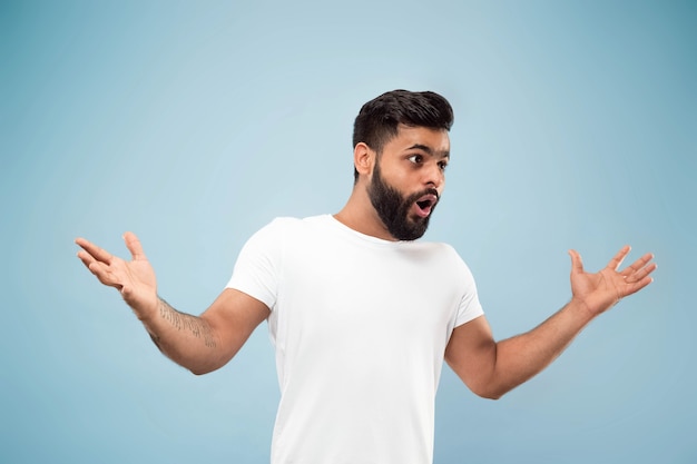 Half-length close up portrait of young man in white shirt on blue wall