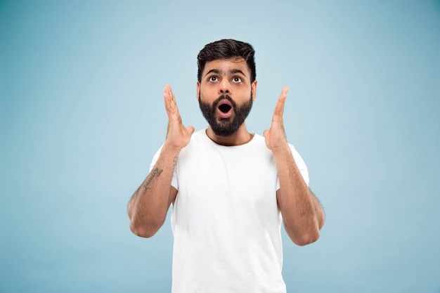 Half-length close up portrait of young man in white shirt on blue wall