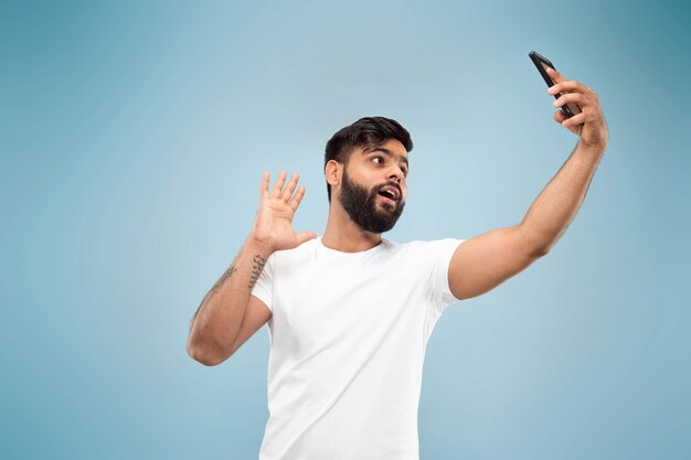 Half-length close up portrait of young man in white shirt on blue wall