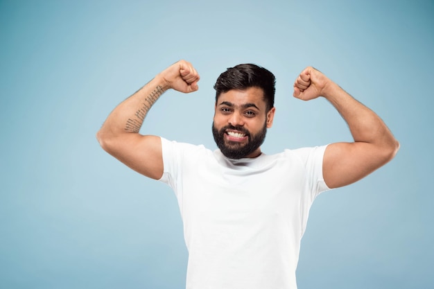 Free photo half-length close up portrait of young man in white shirt on blue wall