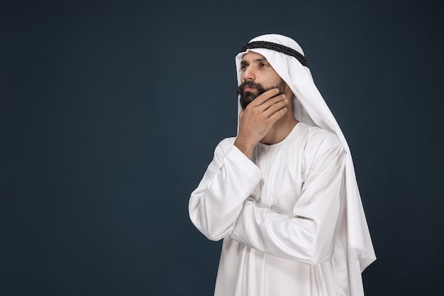 Free photo half-length portrait of arabian saudi businessman. young male model standing and looks thoughtful. concept of business, finance, facial expression, human emotions.