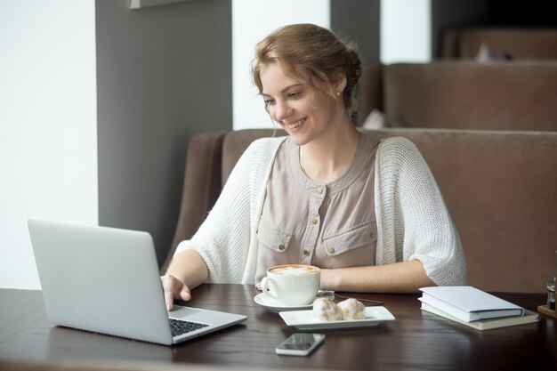 Half-length portrait of happy woman using laptop in cafe