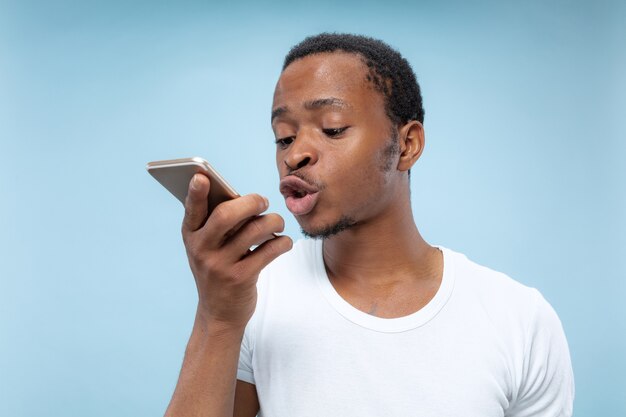 Half-length portrait of young african-american man in white shirt on blue space