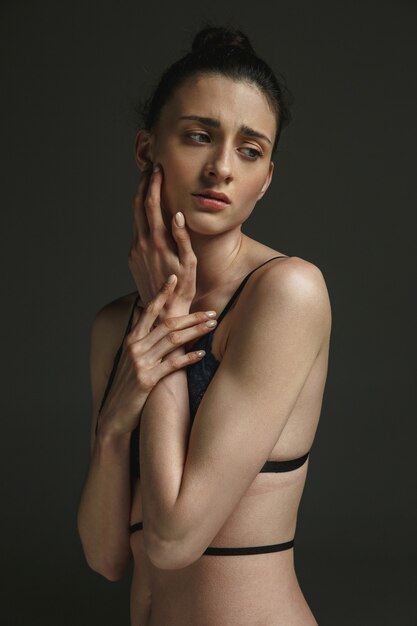 Half-length portrait of young sad woman in underwear on dark studio wall