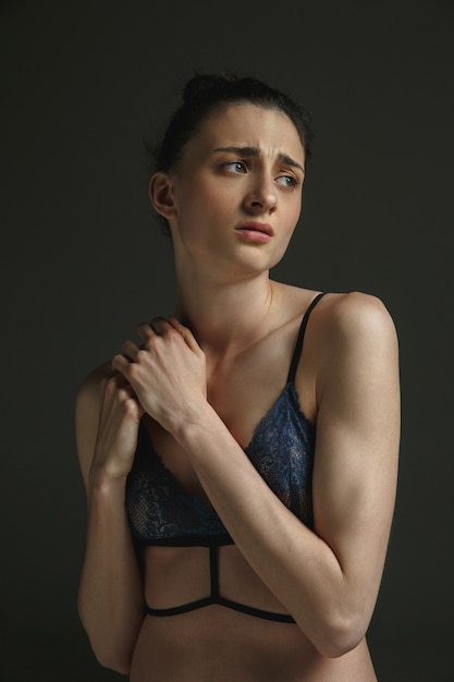 Half-length portrait of young sad woman in underwear on dark studio wall