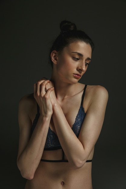 Half-length portrait of young sad woman in underwear on dark wall. Sadness, depression and addiction. Concept of human emotions, feminism, woman's problems and rights, mental health.