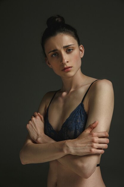 Half-length portrait of young sad woman in underwear on dark wall. Sadness, depression and addiction. Concept of human emotions, feminism, woman's problems and rights, mental health.