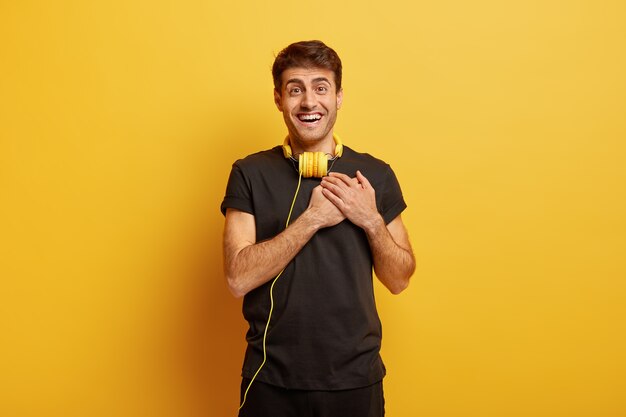 Half length shot of happy European man makes gratitude gesture, touched by romantic song