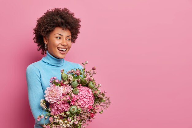 Half length shot of nice attractive Afro American woman  holds bunch of fresh flowers