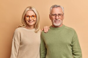 Free photo half length shot of pleased middle aged woman and man smile pleasantly wear jumpers and spectacles