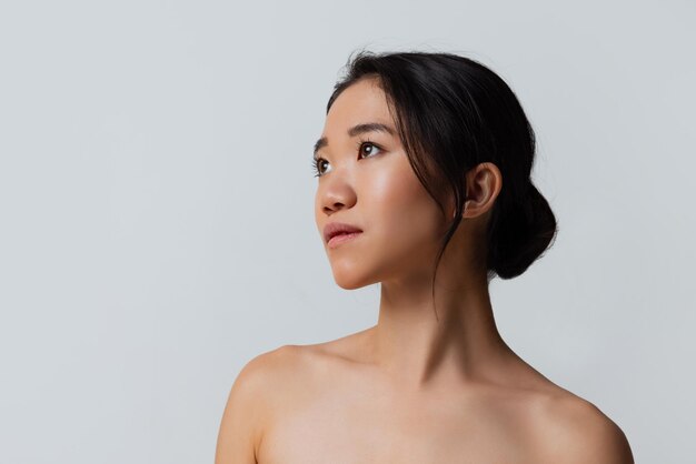 Half length studio portrait of tender young woman posing looking away isolated over gray background