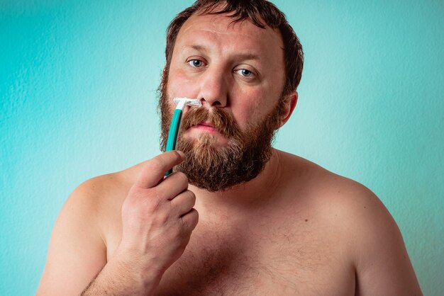 Half-naked Caucasian bearded man shaving with a serious face expression