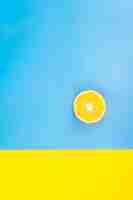 Free photo half of an orange on a blue and yellow background flat lay minimalism