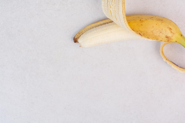 Half peeled single banana on white surface.