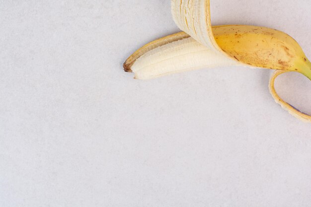 Half peeled single banana on white surface.