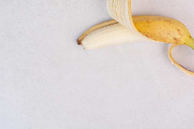 Половина очищенного одного банана на белой поверхности.