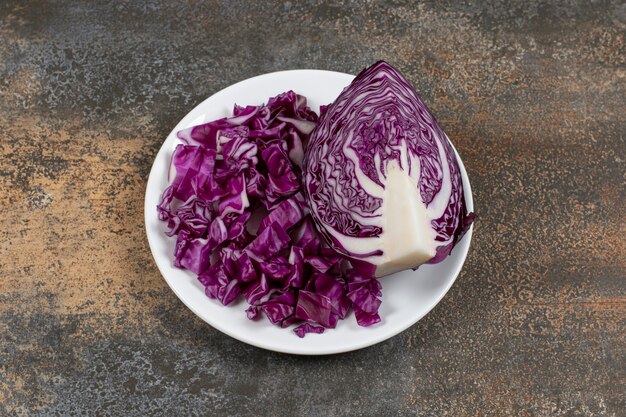 Half a piece of red cabbage next to finely chopped cabbage, on the plate , on the marble surface