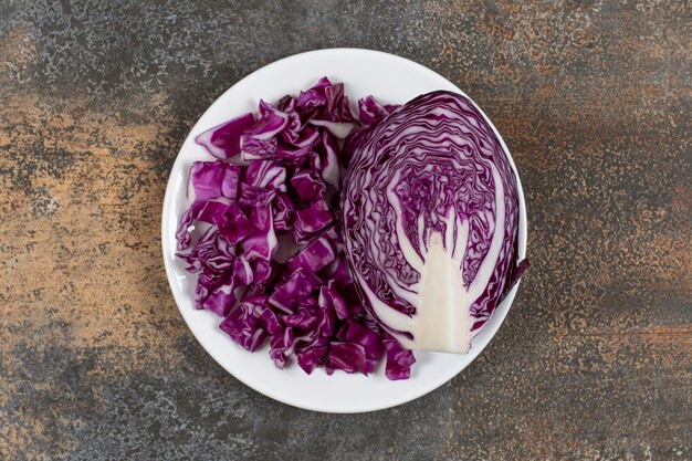 Half a piece of red cabbage next to finely chopped cabbage, on the plate , on the marble surface