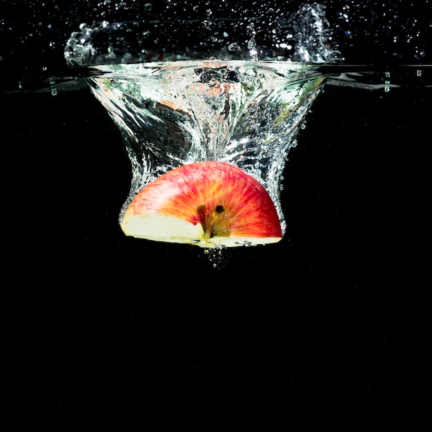 Free photo half red apple falling into water with bubbles against black background