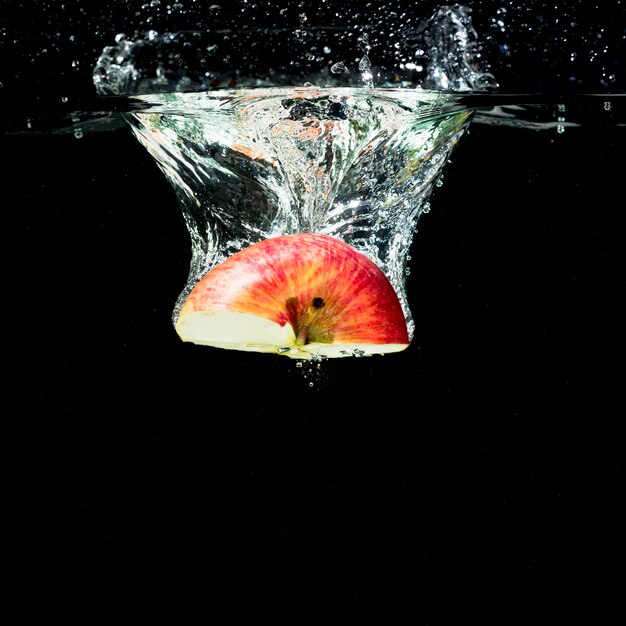 Half red apple falling into water with bubbles against black background